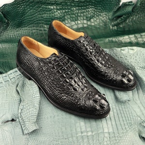 May include: Two black leather shoes with a crocodile pattern. The shoes have laces and are on a light blue background.