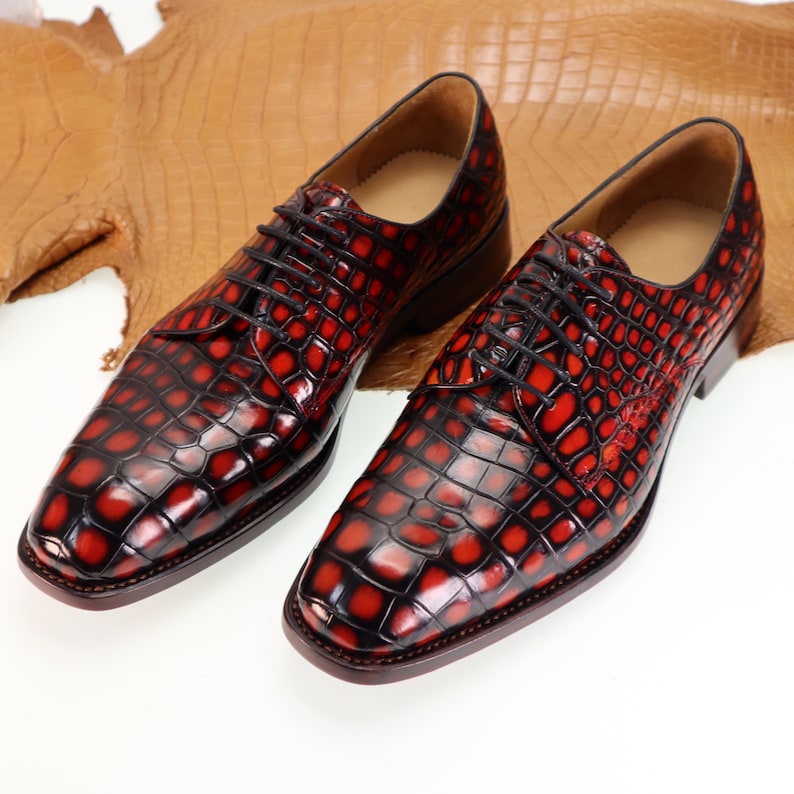 May include: A pair of red and black leather dress shoes with a crocodile pattern. The shoes have lace-up closures and a pointed toe.
