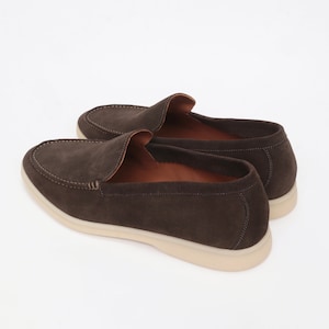 Op de afbeelding: Een paar bruine su&egrave;de loafers met een witte rubberen zool. De loafers hebben een slip-on ontwerp en een licht puntige neus.