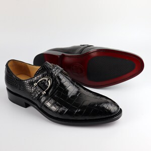 May include: Black leather dress shoes with a crocodile pattern and a silver buckle. The shoes have a pointed toe and a low heel.