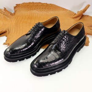 May include: A pair of black leather lace-up shoes with a crocodile pattern. The shoes have a thick, black sole and a rounded toe.