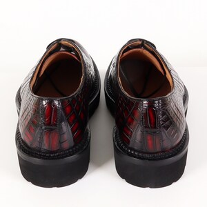 May include: A pair of black leather shoes with a red crocodile pattern. The shoes have a lace-up closure and a thick rubber sole.