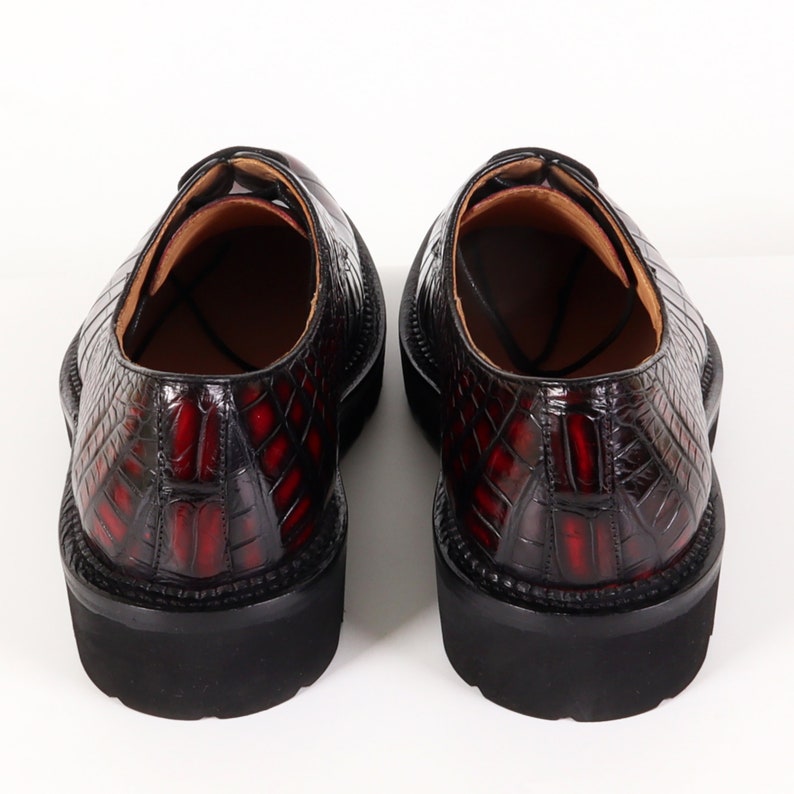 May include: A pair of black leather shoes with a red crocodile pattern. The shoes have a lace-up closure and a thick rubber sole.