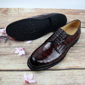 Peut inclure: Une paire de chaussures habill&eacute;es en cuir marron avec un motif crocodile. Les chaussures ont une fermeture &agrave; lacets et une semelle en caoutchouc noir.