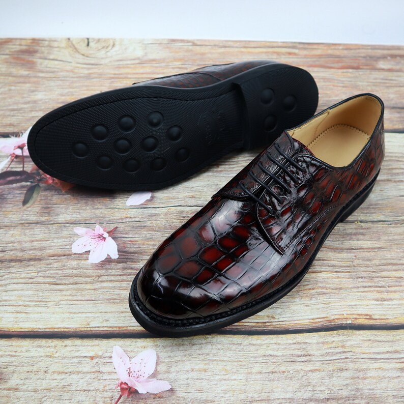 Peut inclure: Une paire de chaussures habill&eacute;es en cuir marron avec un motif crocodile. Les chaussures ont une fermeture &agrave; lacets et une semelle en caoutchouc noir.