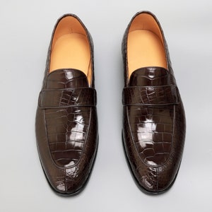 May include: A pair of brown leather loafers with a crocodile pattern. The loafers have a pointed toe and a slip-on design.