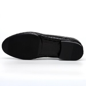 May include: Black leather dress shoe with a textured, crocodile-like pattern. The sole is black and smooth. The shoe has a rounded toe and a low heel. The shoe is designed for formal occasions.