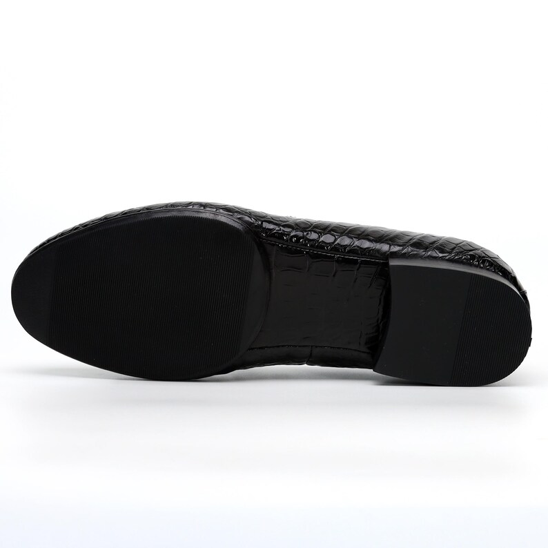 May include: Black leather dress shoe with a textured, crocodile-like pattern. The sole is black and smooth. The shoe has a rounded toe and a low heel. The shoe is designed for formal occasions.