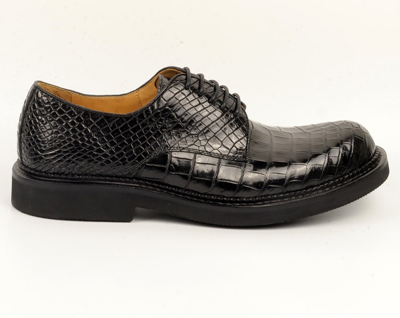 May include: Black leather dress shoes with a crocodile pattern. The shoes have a lace-up closure and a thick sole.