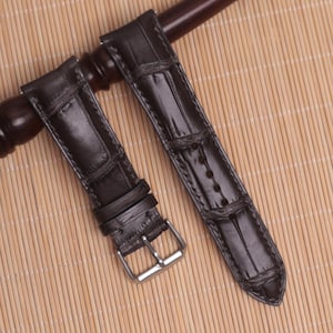 May include: Two brown leather watch straps with a crocodile pattern. One strap has a silver buckle.