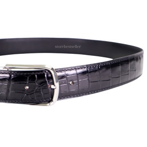 May include: A black leather belt with a crocodile pattern and a silver buckle. The belt is shown in a close-up view.