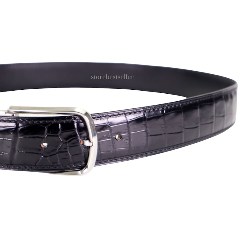 May include: A black leather belt with a crocodile pattern and a silver buckle. The belt is shown in a close-up view.