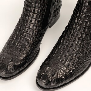 May include: A pair of black crocodile leather boots with a pointed toe and a slight heel. The boots have a textured, alligator-like pattern.