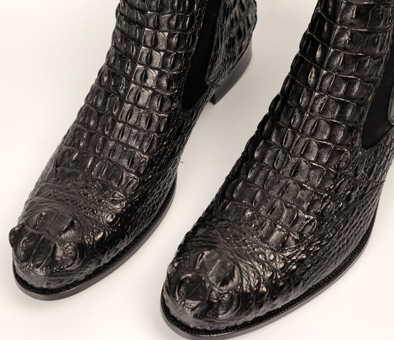 May include: A pair of black crocodile leather boots with a pointed toe and a slight heel. The boots have a textured, alligator-like pattern.