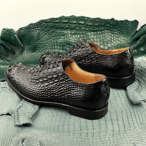 May include: Two black leather shoes with a crocodile pattern on a green crocodile skin background.