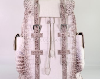 May include: White leather backpack with crocodile embossed pattern and multiple straps and buckles. The backpack has a drawstring closure and two side pockets.