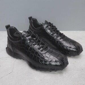 Puede incluir: Un par de zapatillas negras con un patr&oacute;n texturizado similar al de la piel de cocodrilo. Los zapatos tienen cordones negros y una suela gruesa negra. Las zapatillas est&aacute;n dise&ntilde;adas para uso casual.
