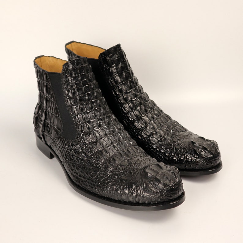 May include: A pair of black leather ankle boots with a crocodile pattern. The boots have a pointed toe and a low heel.