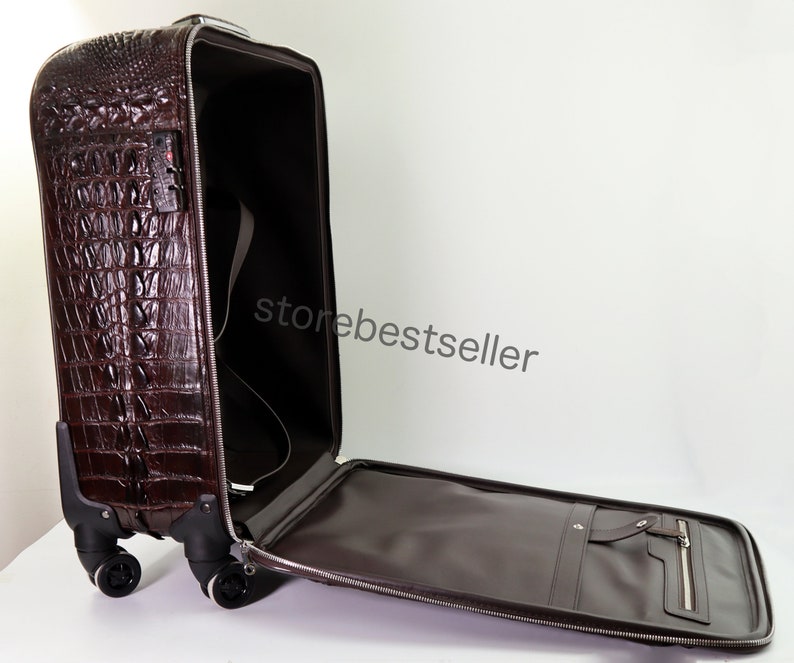 May include: A brown crocodile-embossed leather suitcase with a zippered pocket on the front and a handle on the top. The suitcase is open and the interior is lined with brown fabric. The suitcase has four wheels and a retractable handle.