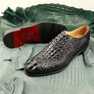 May include: Black leather dress shoes with crocodile pattern. The shoes are on a green alligator skin background.