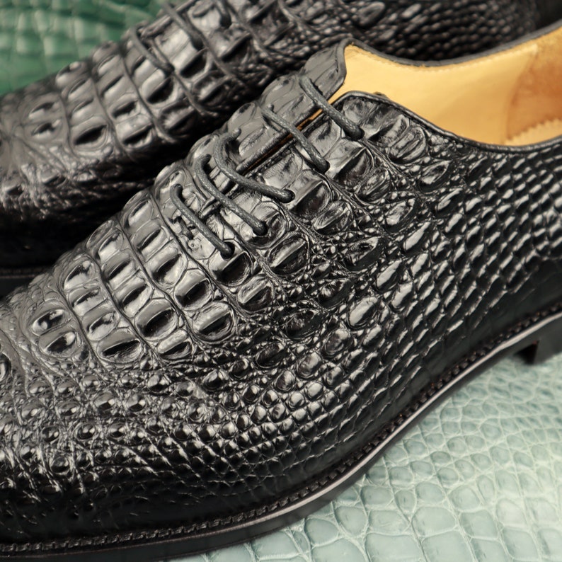May include: Close-up of a pair of black leather shoes with a crocodile skin pattern. The shoes have a lace-up closure and a polished finish.