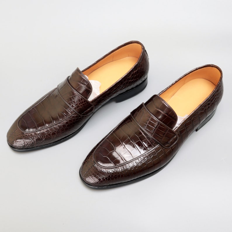 May include: A pair of brown leather loafers with a crocodile pattern. The loafers have a pointed toe and a slip-on design.