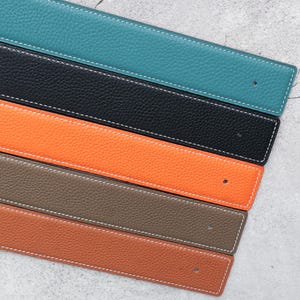 Op de afbeelding: Close-up van leren riemen in verschillende kleuren: turquoise, zwart, oranje, bruin en roest. Elke riem heeft witte stiksels en een klein gaatje. Het leer heeft een getextureerde korrel. De afmetingen zijn in centimeters.