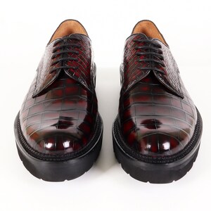 May include: A pair of burgundy leather lace-up shoes with a crocodile-embossed pattern. The shoes have a thick black rubber sole.