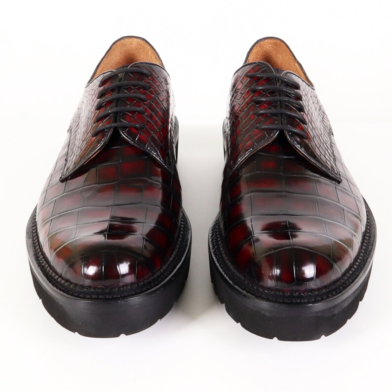 May include: A pair of burgundy leather lace-up shoes with a crocodile-embossed pattern. The shoes have a thick black rubber sole.
