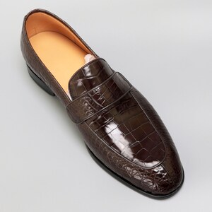 May include: A brown leather loafer with a crocodile pattern. The loafer has a pointed toe and a slip-on design.