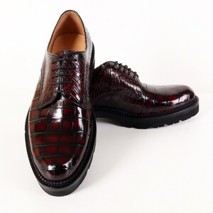May include: A pair of dark red leather shoes with a crocodile pattern. The shoes have laces and a rounded toe.