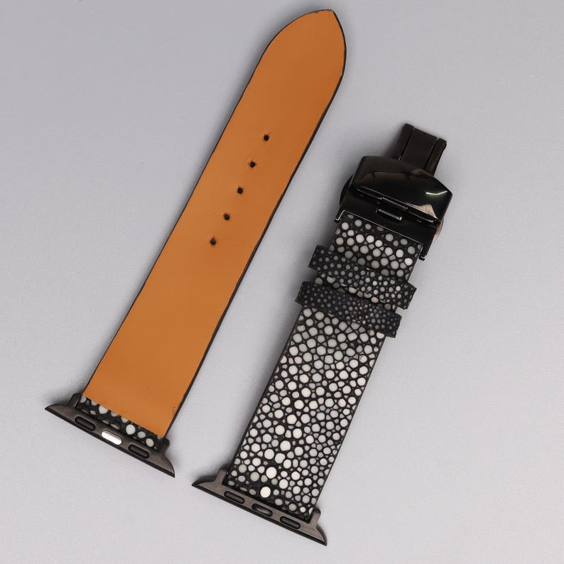 Puede incluir: Una correa de reloj con un cierre negro y una correa de material moteado blanco y negro. La otra correa es de cuero marr&oacute;n claro con una hebilla negra. Las correas de reloj se muestran sobre un fondo gris claro.