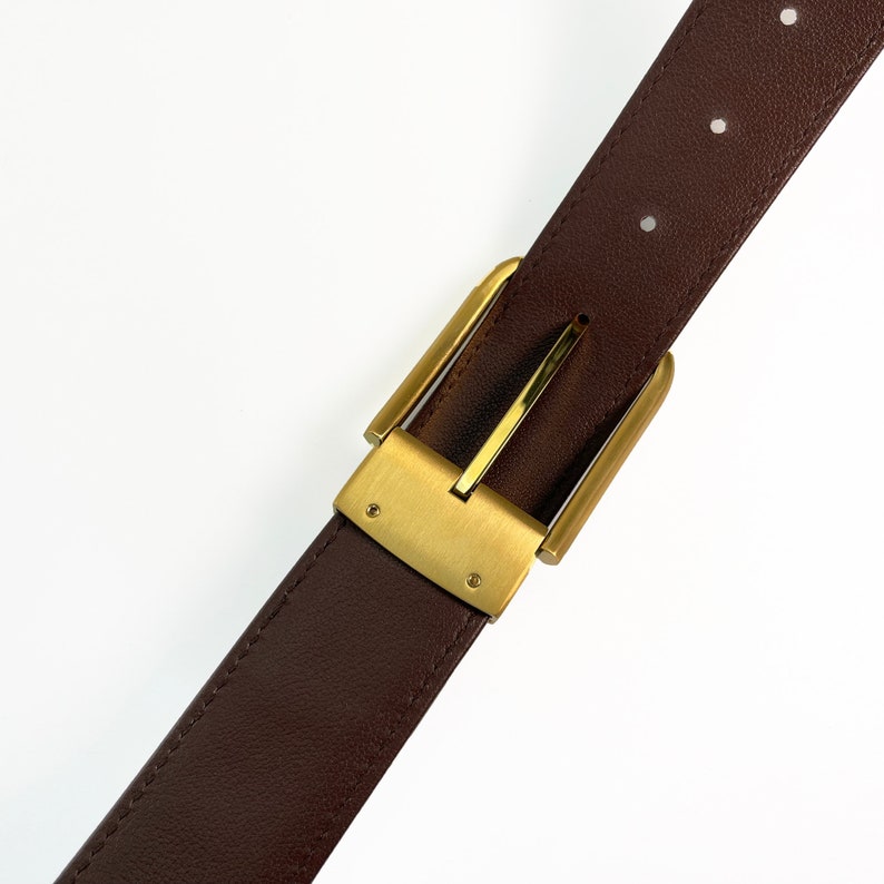 May include: A brown leather belt with a gold metal buckle. The buckle has a simple design with a smooth finish.