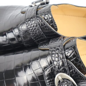 May include: Two black leather shoes with a crocodile skin pattern and silver buckles. The shoes have a pointed toe and a low heel.