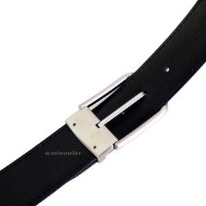 May include: A black leather belt with a silver buckle. The buckle has a smooth, polished finish and a simple design.