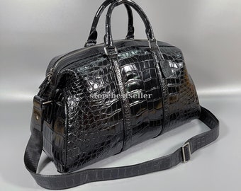 May include: Black crocodile leather travel bag with a top handle and a shoulder strap. The bag has a zipper closure and a front pocket.