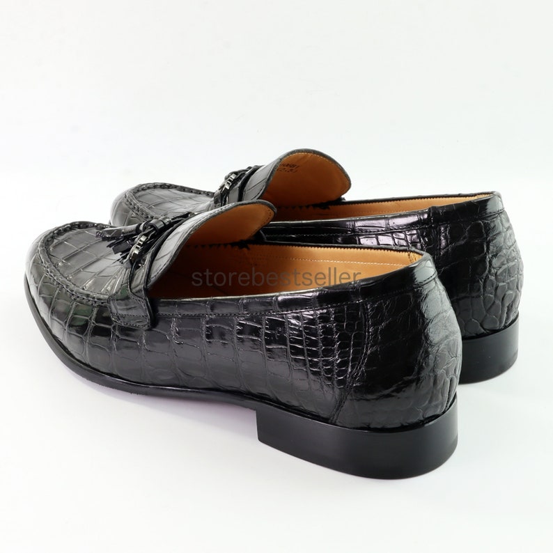 May include: Black leather loafers with a crocodile pattern and tassel detail.