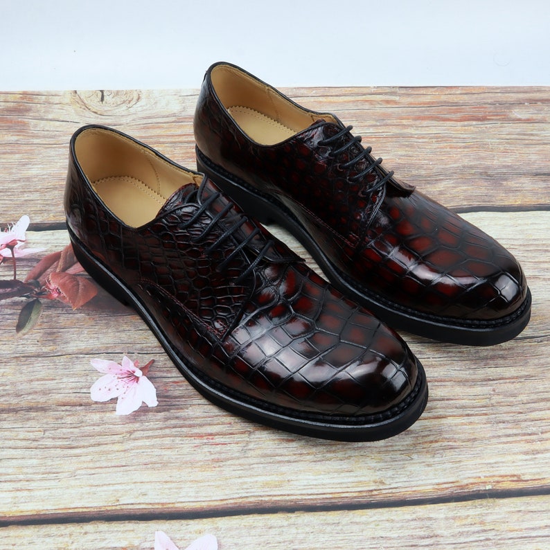 Peut inclure: Deux paires de chaussures &agrave; lacets en cuir marron fonc&eacute; avec un motif crocodile. Les chaussures ont une semelle en caoutchouc noir.