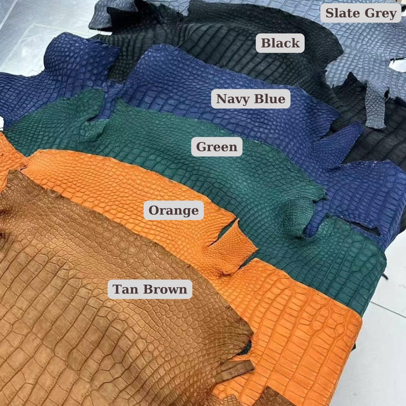 May include: A collection of textured leather swatches in various colors, including tan brown, orange, green, navy blue, black, and slate grey. Each swatch has a reptile-like pattern. The colors are labeled with white rectangular tags.