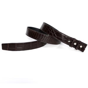 May include: A dark brown belt with a crocodile skin pattern. The belt is made of leather and has a black interior. The belt has a buckle with two silver-coloured snaps.