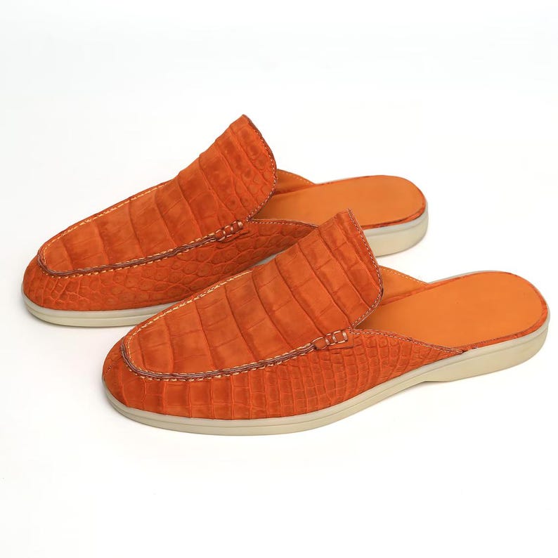 May include: A pair of orange leather slip-on shoes with a crocodile texture. The shoes have a rounded toe and a light-colored sole. The stitching is visible along the seams, and the interior is orange.