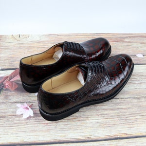 Peut inclure: Une paire de chaussures habill&eacute;es en cuir marron avec un motif crocodile. Les chaussures ont des lacets et sont sur une surface en bois.
