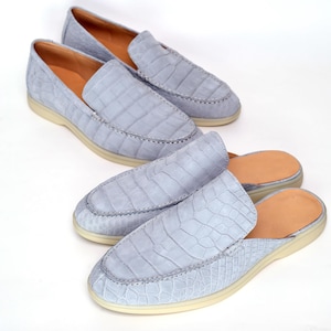 May include: Two pairs of light blue alligator-textured leather loafers. One pair is a closed-toe design, and the other is a mule-style with an open back. Both have light-colored soles and tan leather insoles.