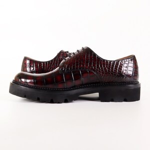 May include: A pair of burgundy leather lace-up shoes with a crocodile-embossed pattern. The shoes have a chunky black rubber sole.