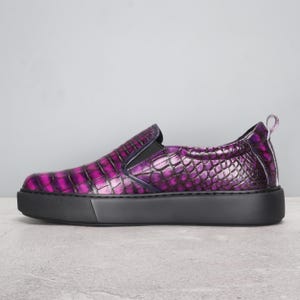 May include: A slip-on shoe with a textured, purple, crocodile-like pattern. The shoe has a black sole and a small pull tab at the heel. The shoe is a size 9.