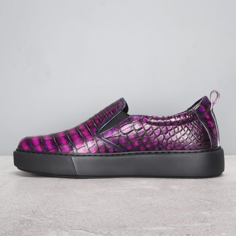 May include: A slip-on shoe with a textured, purple, crocodile-like pattern. The shoe has a black sole and a small pull tab at the heel. The shoe is a size 9.
