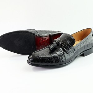 May include: Black leather loafers with a crocodile pattern and a tassel detail. The loafers have a pointed toe and a low heel.