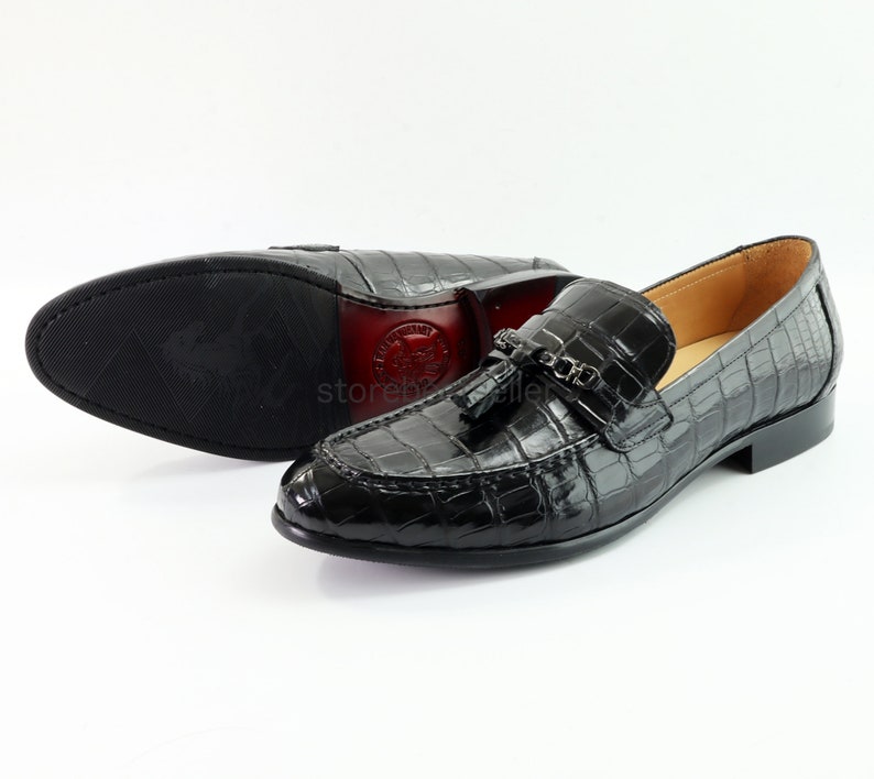 May include: Black leather loafers with a crocodile pattern and a tassel detail. The loafers have a pointed toe and a low heel.