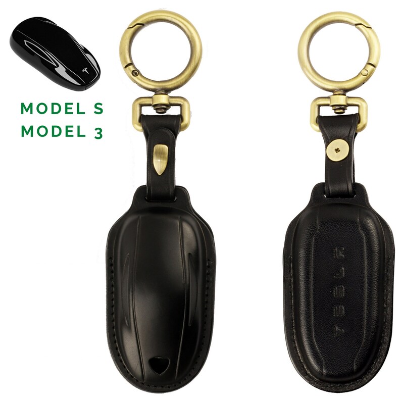 May include: Black leather key fob with a gold metal ring and clasp. The fob is shaped like a Tesla Model S or Model 3 car key. The text "MODEL S MODEL 3" is printed in green on a white background.