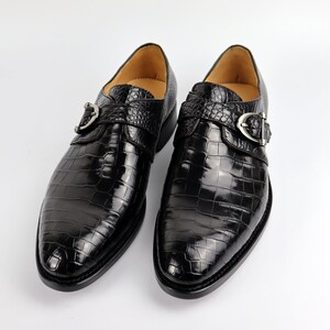 May include: A pair of black leather dress shoes with a crocodile pattern. The shoes have a buckle fastening and a pointed toe.